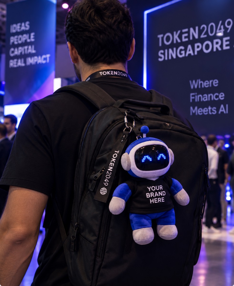 A branded plushie clipped to a backpack on the TOKEN2049 show floor